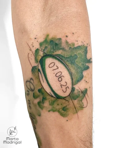 Tatouage aquarelle d'un ballon de rugby avec une date, sur l'avant-bras, à Toulouse