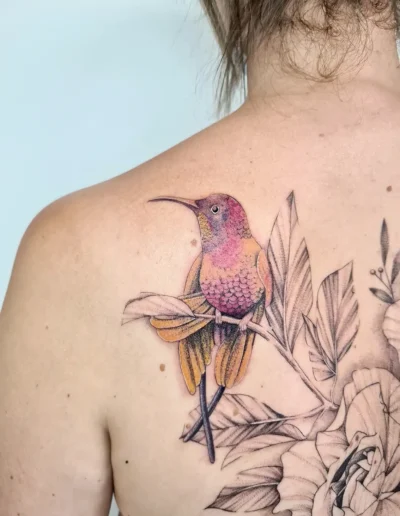 Tatouage couleur d'un colibri parmi des fleurs, sur l'omoplate, à Toulouse