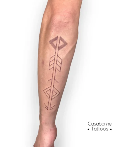 Tatouage d'une flèche géométrique inspirée du symbole Harakbut, sur l'avant-bras, à Toulouse