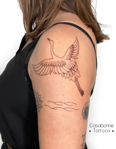 Tatouage ligne fine d'une grue et de vagues, sur le bras, à Toulouse