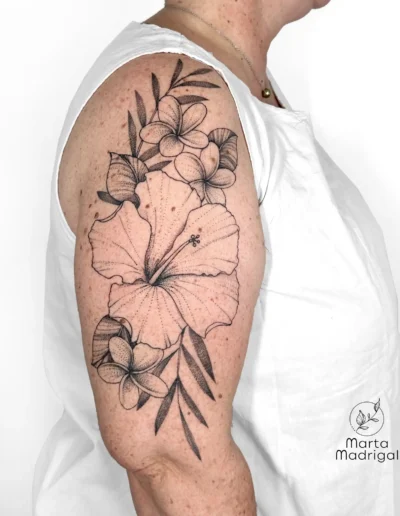 Tatouage tropical d'hibiscus et frangipanier sur le haut du bras, a Toulouse