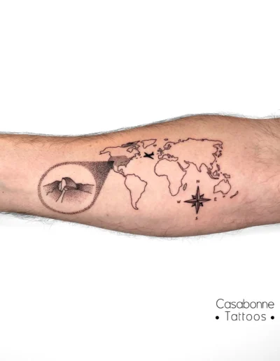 Tatouage ligne fine d'une mappemonde avec une boussole et un détail d'oiseau, sur l'avant-bras, à Toulouse