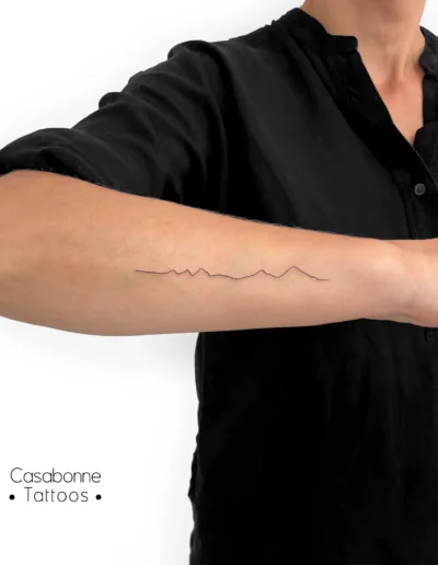 Tatouage ligne fine d'une chaîne de montagnes, sur le bras, à Toulouse