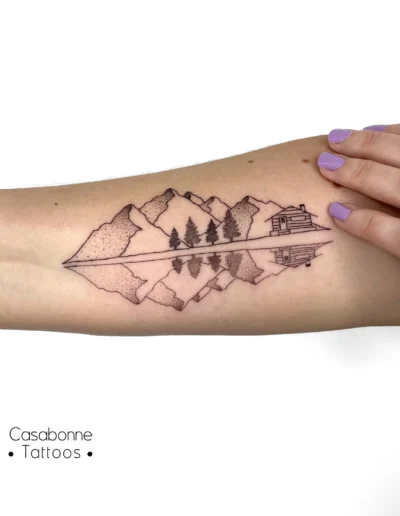 Tatouage ligne fine de montagnes avec leur reflet dans l'eau, sur l'avant-bras, à Toulouse