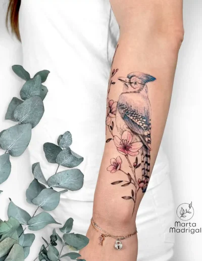 Tatouage d'un oiseau bleu parmi des fleurs, sur l'avant-bras, à Toulouse