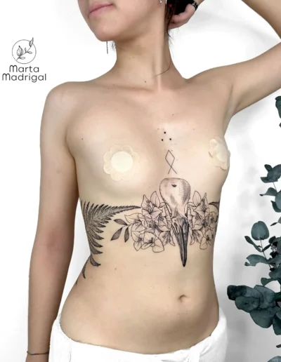 Tatouage d'un crâne d'oiseau stylisé entouré de fleurs, sous la poitrine, à Toulouse
