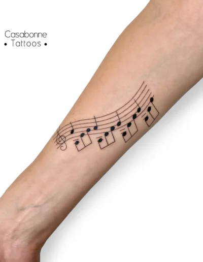 Tatouage ligne fine d'une portée musicale, sur l'avant-bras, à Toulouse