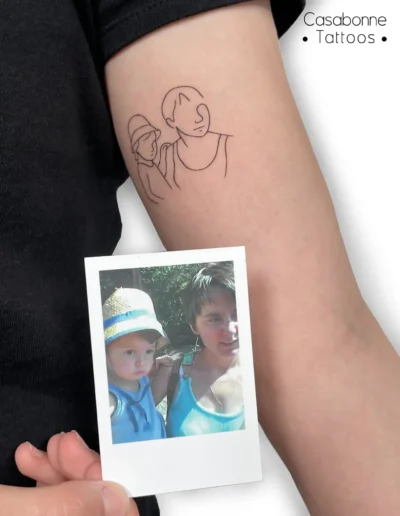 Tatouage ligne fine d'un portrait mère-fille réalisé à partir d'une photo, vue rapprochée, sur le bras, à Toulouse
