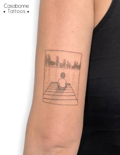 Tatouage ligne fine d'une scène illustrée encadrée, sur le bras, à Toulouse