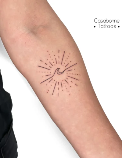 Tatouage d'un soleil rayonnant avec une vague, sur l'avant-bras, à Toulouse