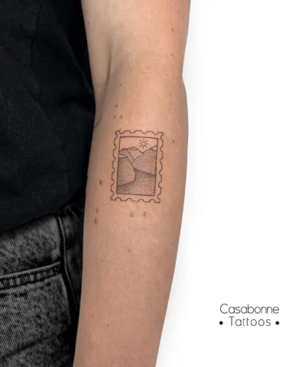 Tatouage en forme de timbre postal avec un paysage de fjords, sur le bras, à Toulouse