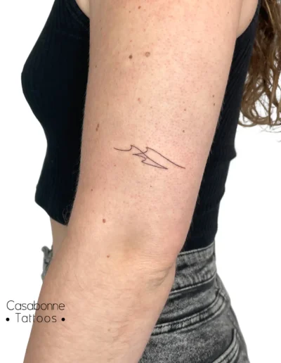 Tatouage ligne fine d'une vague stylisée, sur l'avant-bras, à Toulouse