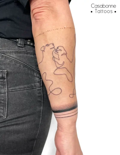 Tatouage ligne fine de deux visages entrelacés, sur l'avant-bras, à Toulouse