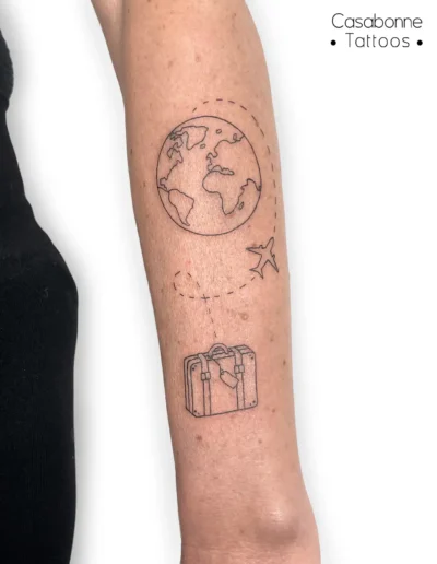 Tatouage sur le thème du voyage : planète Terre, avion et valise, sur l'avant-bras, à Toulouse